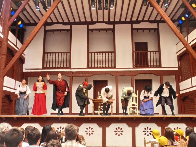 Representación de "El médico a palos", de Molière. Aparecen las actrices y actores saludando al público. Están en un escenario clásico de madera